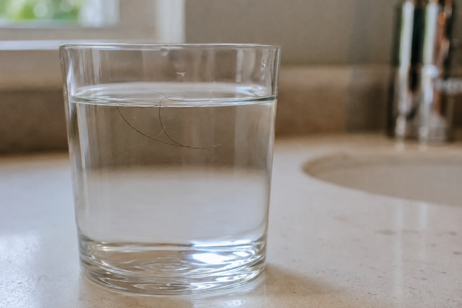 A single hair strand floating in a clear glass of water